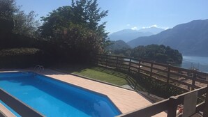 A swimming pool with a wooden deck and a view of mountains and a lake.