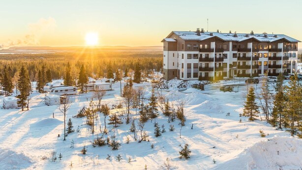 A multi-story building with a symmetrical facade, surrounded by a snowy landscape and sparse trees.