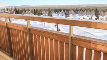 Holzgeländer auf einer Terrasse mit Blick auf eine verschneite Landschaft, Bäume und Gebäude in der Ferne.
