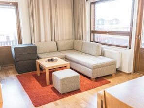 Uma sala de estar moderna com um sofá modular, uma mesinha, um banquinho cinza e um tapete vermelho.