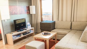 A modern living room with a flat-screen TV, a sofa, a coffee table, and a small ottoman.