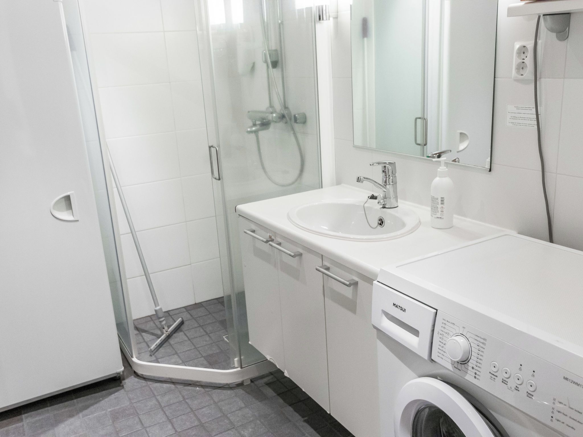 Casa de banho moderna com cabine de duche em vidro, máquina de lavar roupa embutida e lavatório com espelho.