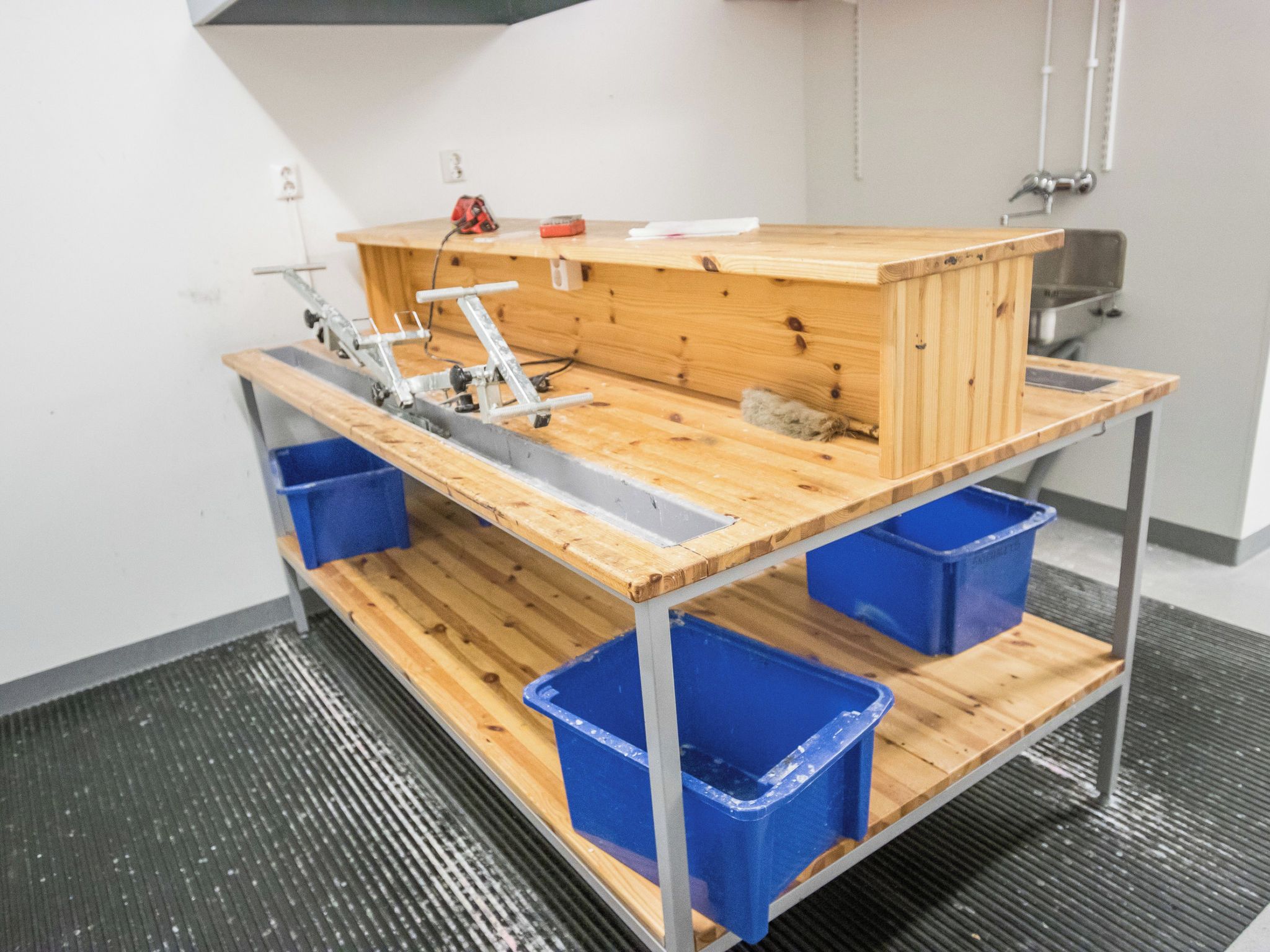 A workshop area with a workbench, blue storage bins, and a power tool.