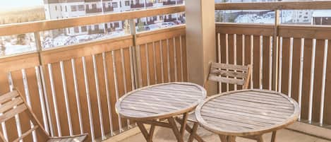 Un balcon doté de deux tables et de chaises en bois, donnant sur un quartier résidentiel composé de plusieurs immeubles.