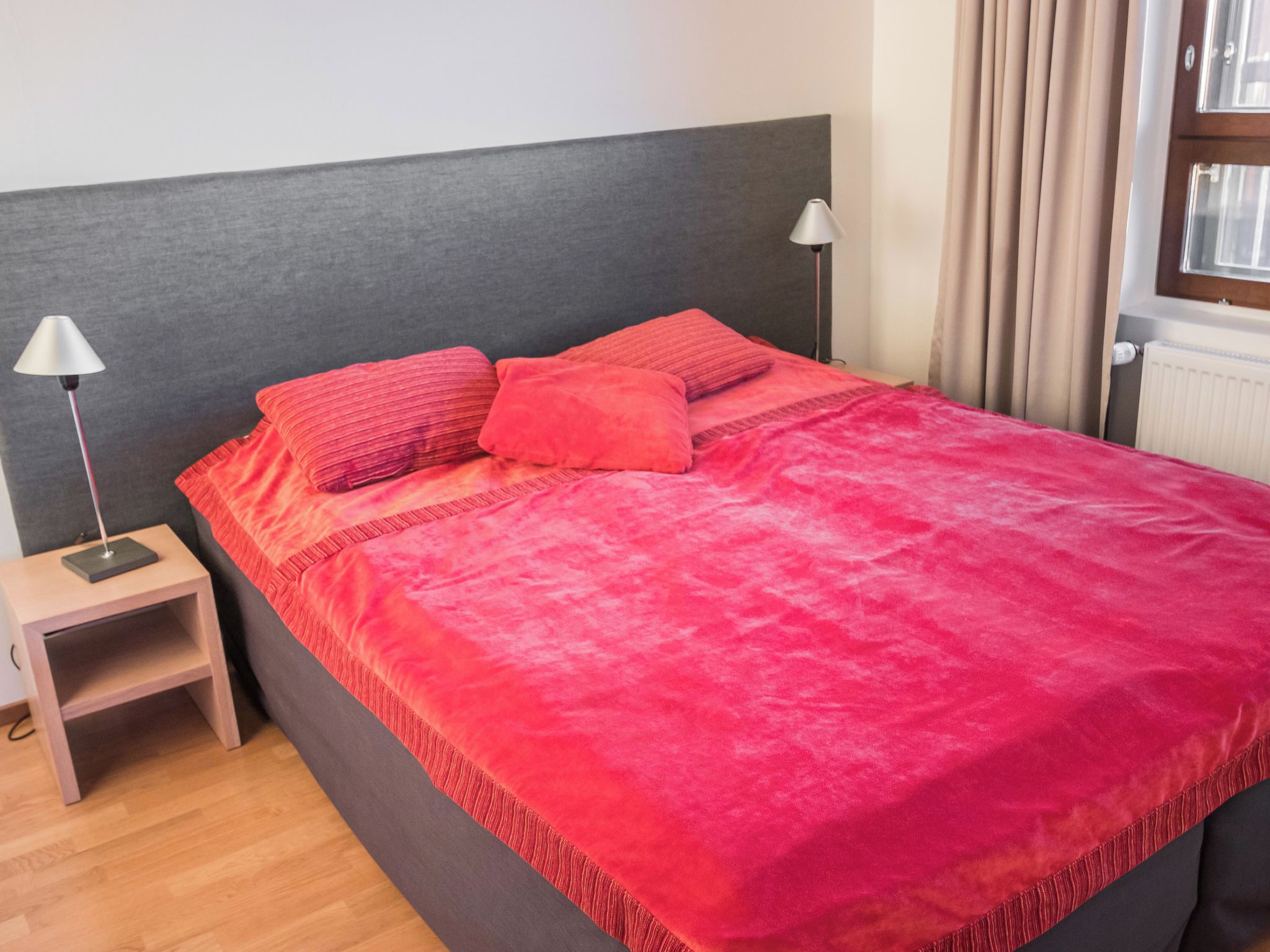 A bed with a grey headboard, two bedside lamps, and a red blanket.
