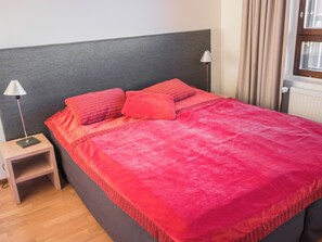 A bed with a grey headboard, two bedside lamps, and a red blanket.