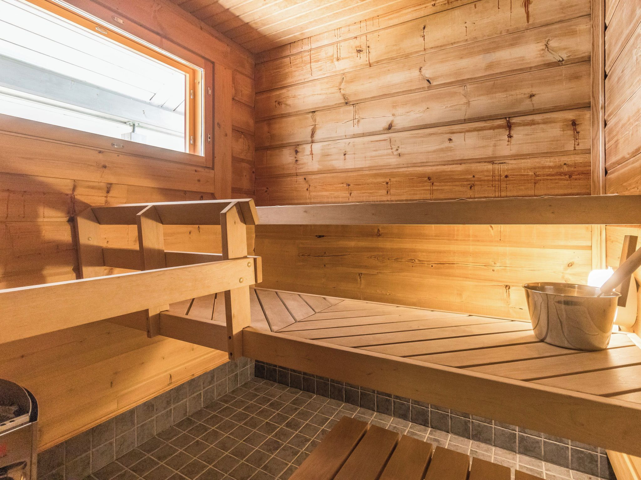 A sauna room with wooden benches, a tiled floor, and a window for natural light.