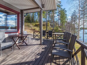 Puinen terassi, jossa on ulkokalusteita, ja josta avautuu näkymä metsäiselle alueelle ja vesistölle.