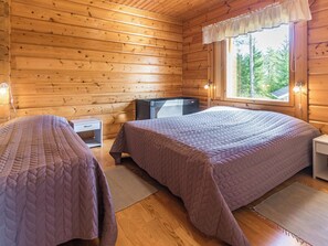A cabin room with two beds, a small table, and a window with a view of trees.