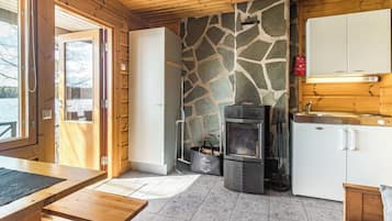 Un interior acogedor de cabaña con una pared de piedra, una chimenea, una mesa de madera y un armario blanco.