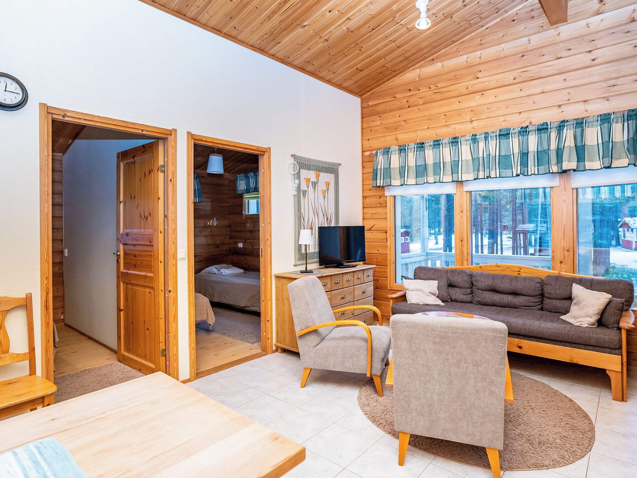 A cozy cabin interior with a wooden ceiling, a sofa, a TV, and a dining area.