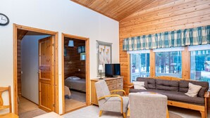 Ein gemütliches Blockhaus-Interieur mit Holzbalkendecke, einer Couch, einem Fernseher und einem Essbereich.