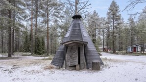 Eine verschneite Holzhütte mit Kegeldach, umgeben von einem Wald.