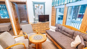 Ein gemütlicher Wohnbereich mit einer Couch, Sesseln, einem Holztisch und einem Fernseher.