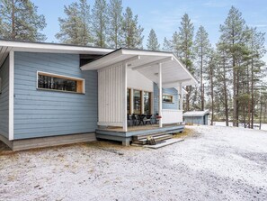 A cabin with a covered porch, a small deck, and a view of a forest.
