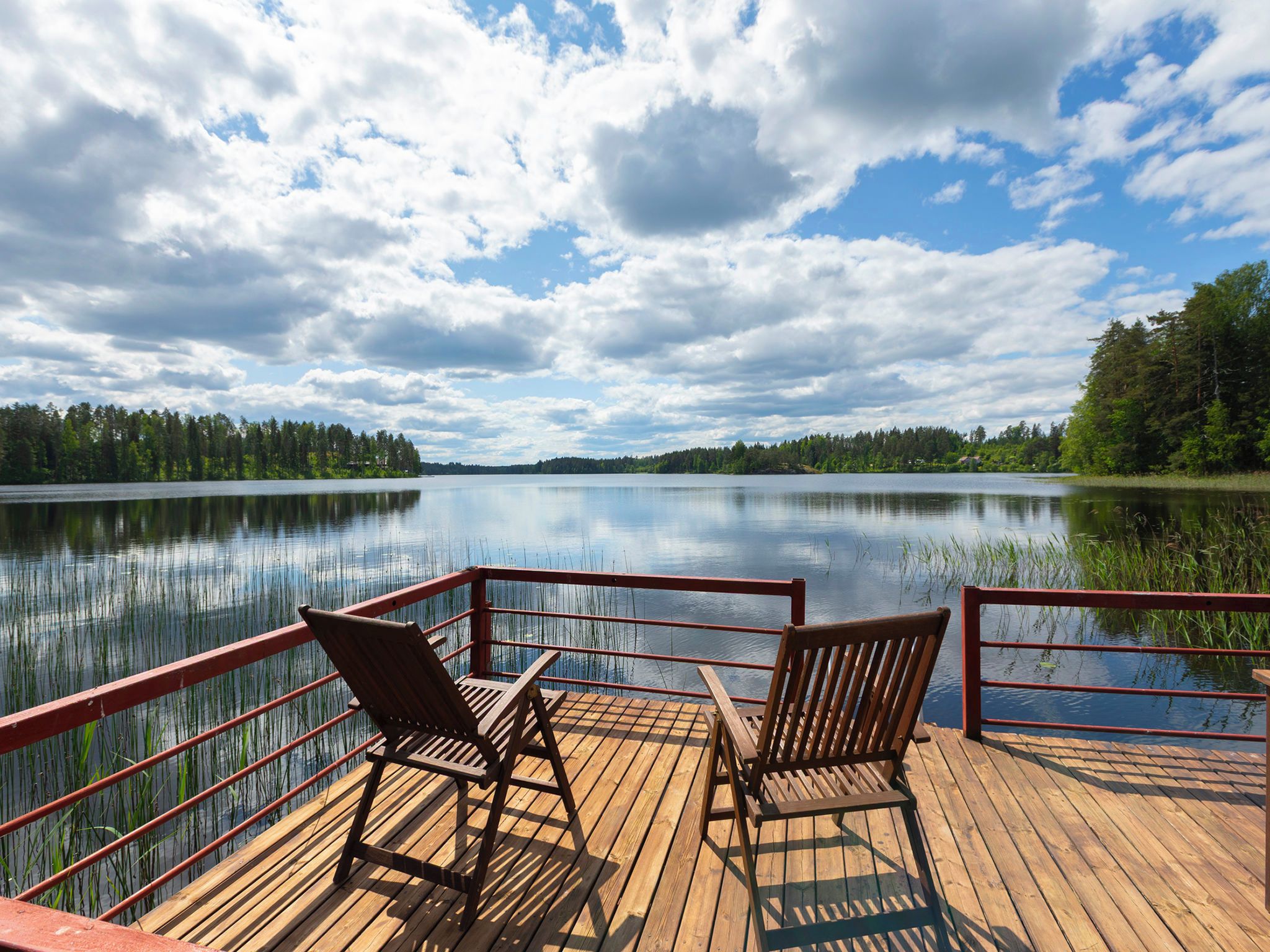 Une terrasse en bois avec deux chaises donnant sur un lac paisible, le tout entouré d’arbres.