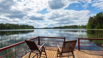 Une terrasse en bois avec deux chaises donnant sur un lac paisible, le tout entouré d’arbres.