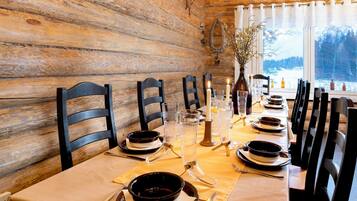 Un intérieur en bois avec une table à manger dressée pour quatre personnes, agrémentée de chaises noires, de verres transparents et d’un vase avec des branches.