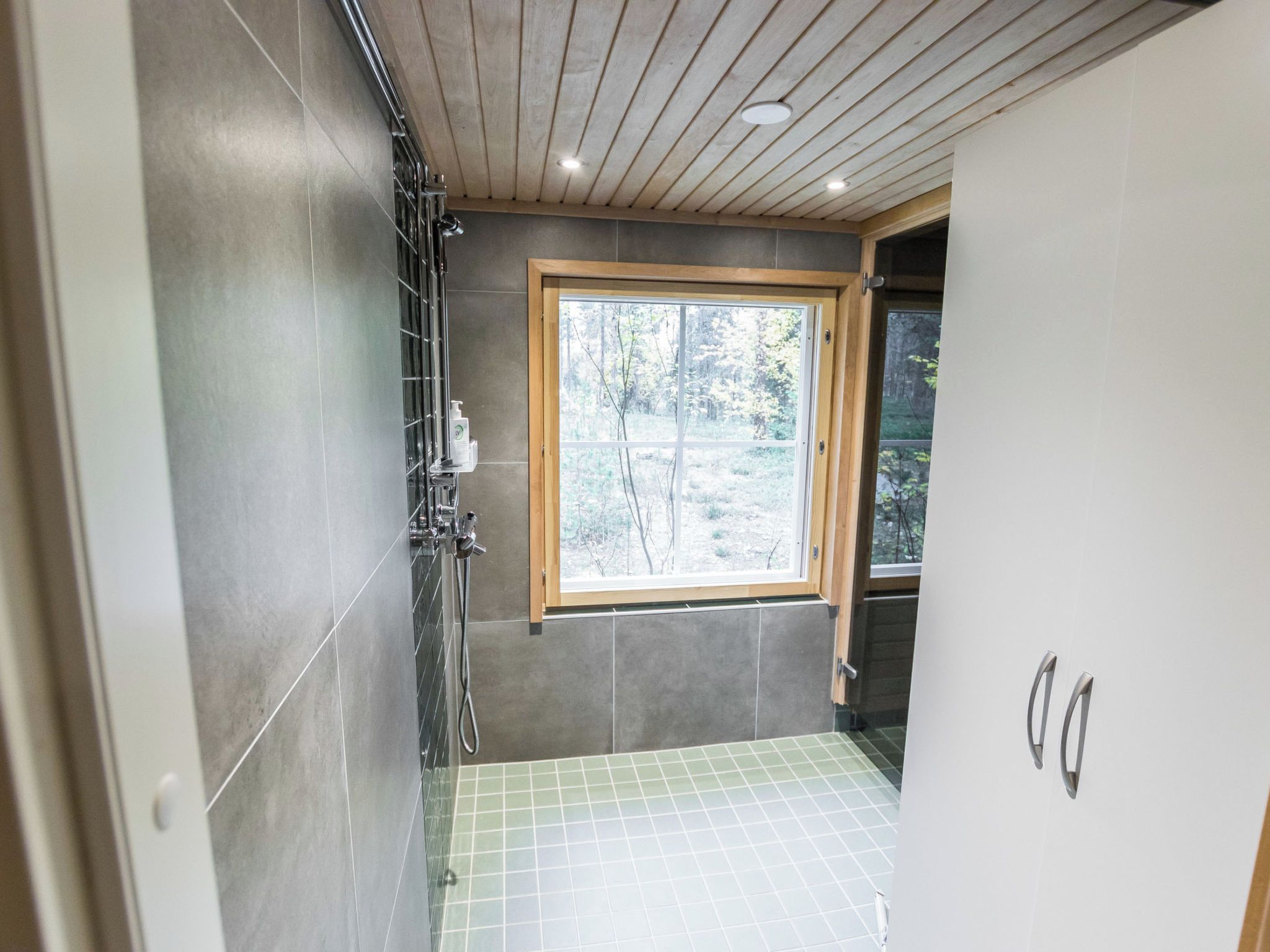 A bathroom with a shower, a window, and a tiled floor.