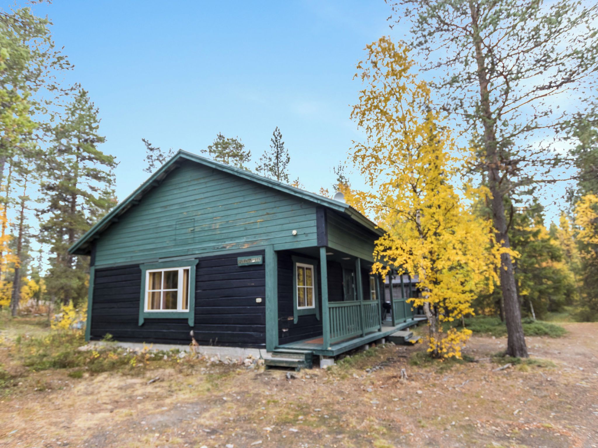 A small, single-story cabin with a porch, surrounded by trees with yellow leaves.