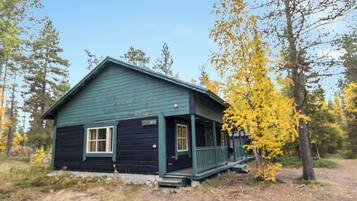 A small, single-story cabin with a porch, surrounded by trees with yellow leaves.