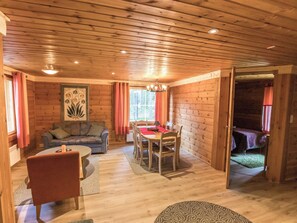 A cozy cabin interior with a dining area, a sofa, and a chair.