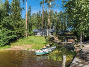 Eine Hütte am Seeufer mit Steg, Boot und kleiner Werkstatt.