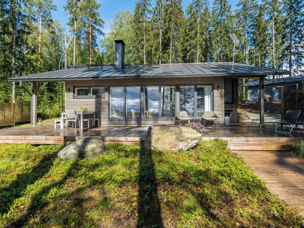 A modern cabin with a deck, large windows, and a view of the forest.