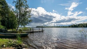Une scène au bord d’un lac, avec une jetée s’avançant dans l’eau, entourée d’arbres et sous un ciel dégagé.