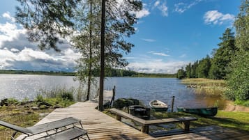 A wooden dock leading to a calm lake with boats, surrounded by trees and greenery.