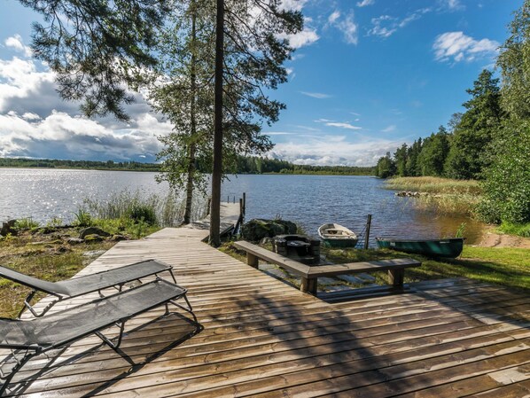 A wooden dock leading to a calm lake with boats, surrounded by trees and greenery.