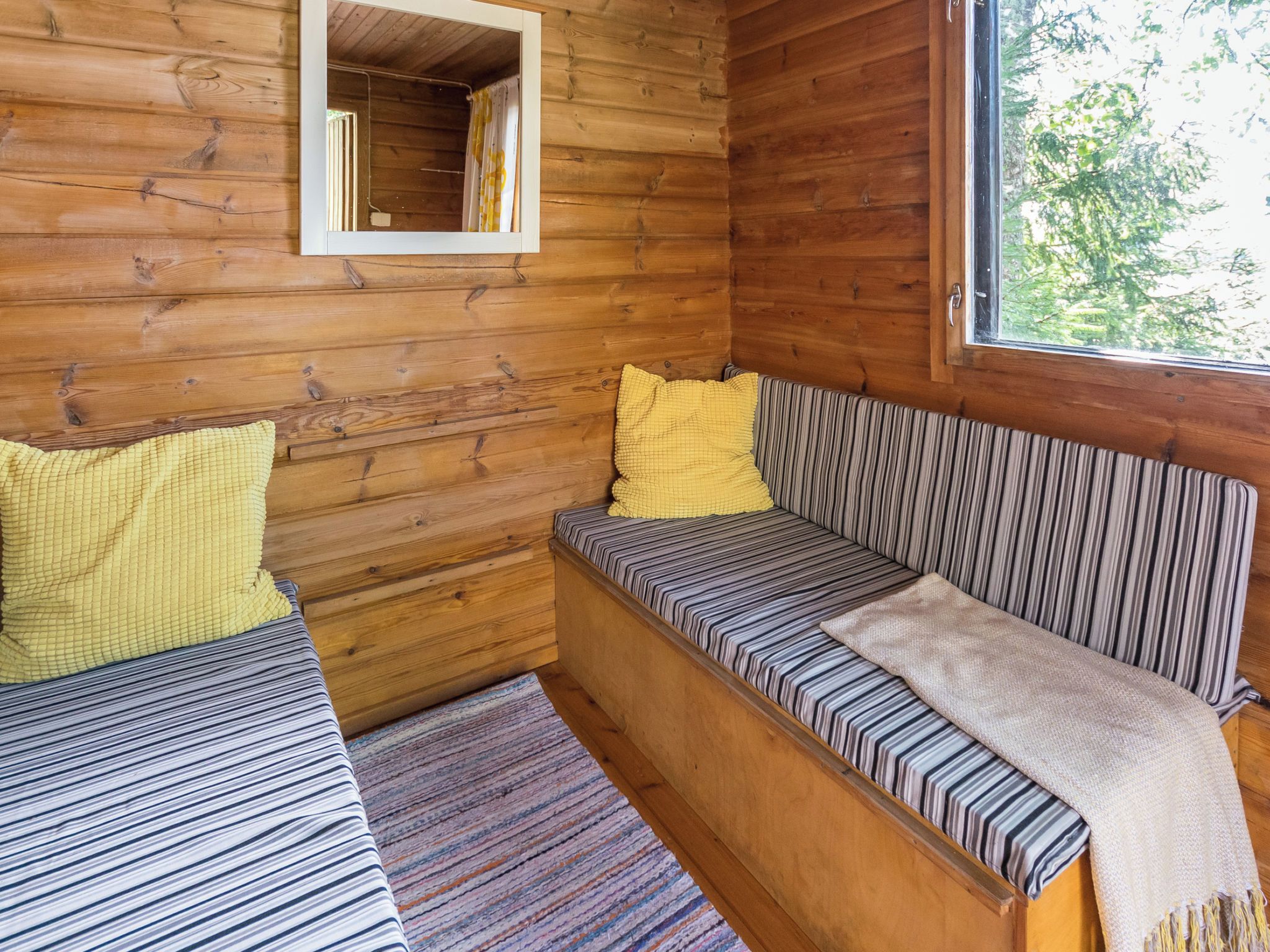 A cabin interior with a wooden wall, a window, a bench, and a bed.