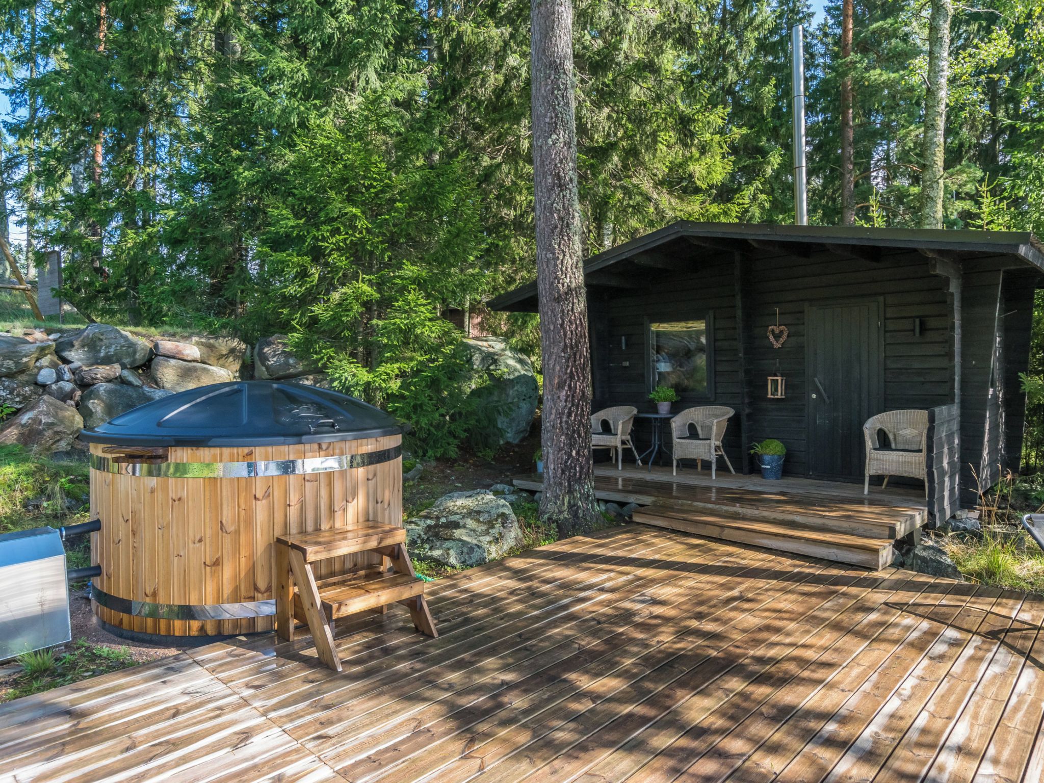 Un terrazzo in legno con idromassaggio, una zona relax coperta con sedie e un muro in pietra.