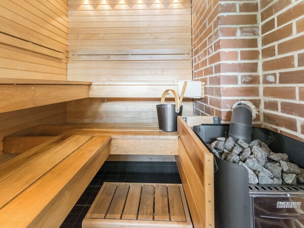 A sauna with wooden benches, a metal bucket, and a stone-filled container, likely for heating.