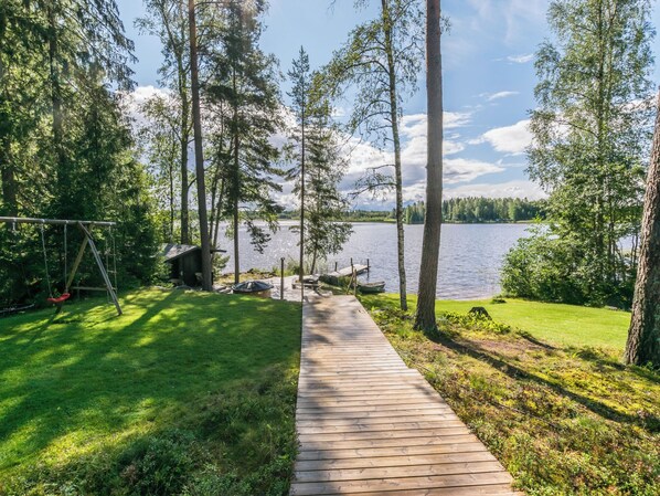 Eine Holzterrasse führt zu einem See mit Bäumen und einer Schaukel.