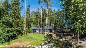 Un chalet au bord du lac, avec un quai, un bateau et une terrasse en bois.