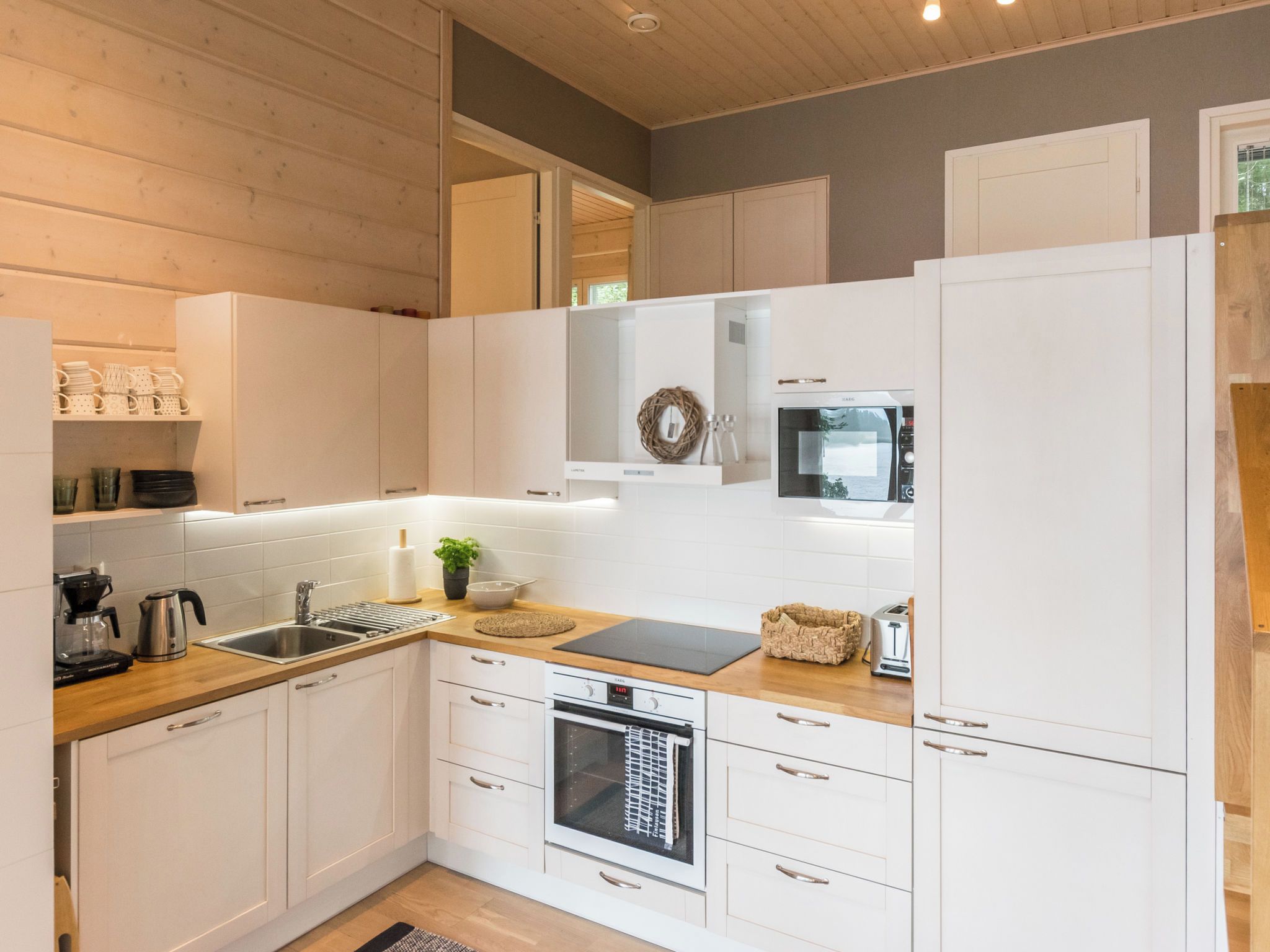 Een moderne keuken met witte kastjes, een inbouwoven, een magnetron en een koffiezetapparaat.