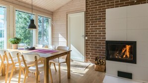 Un salon moderne doté d’une cheminée, d’un plancher en bois et d’un coin repas avec des chaises blanches et une table.