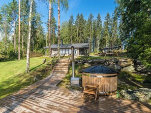 Une terrasse en bois mène à une maison moderne entourée d’une forêt.