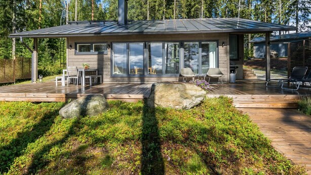 Une maison moderne dotée d’une terrasse en bois, de grandes fenêtres et d’une cheminée.