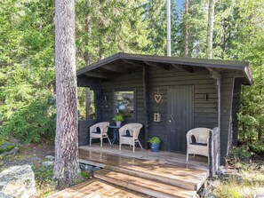 Een houten blokhut met een veranda, twee rieten stoelen en een kleine tafel.