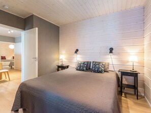 Un dormitorio con una cama grande, dos mesitas de noche y un tocador. Hay una puerta que conduce a otra habitación.