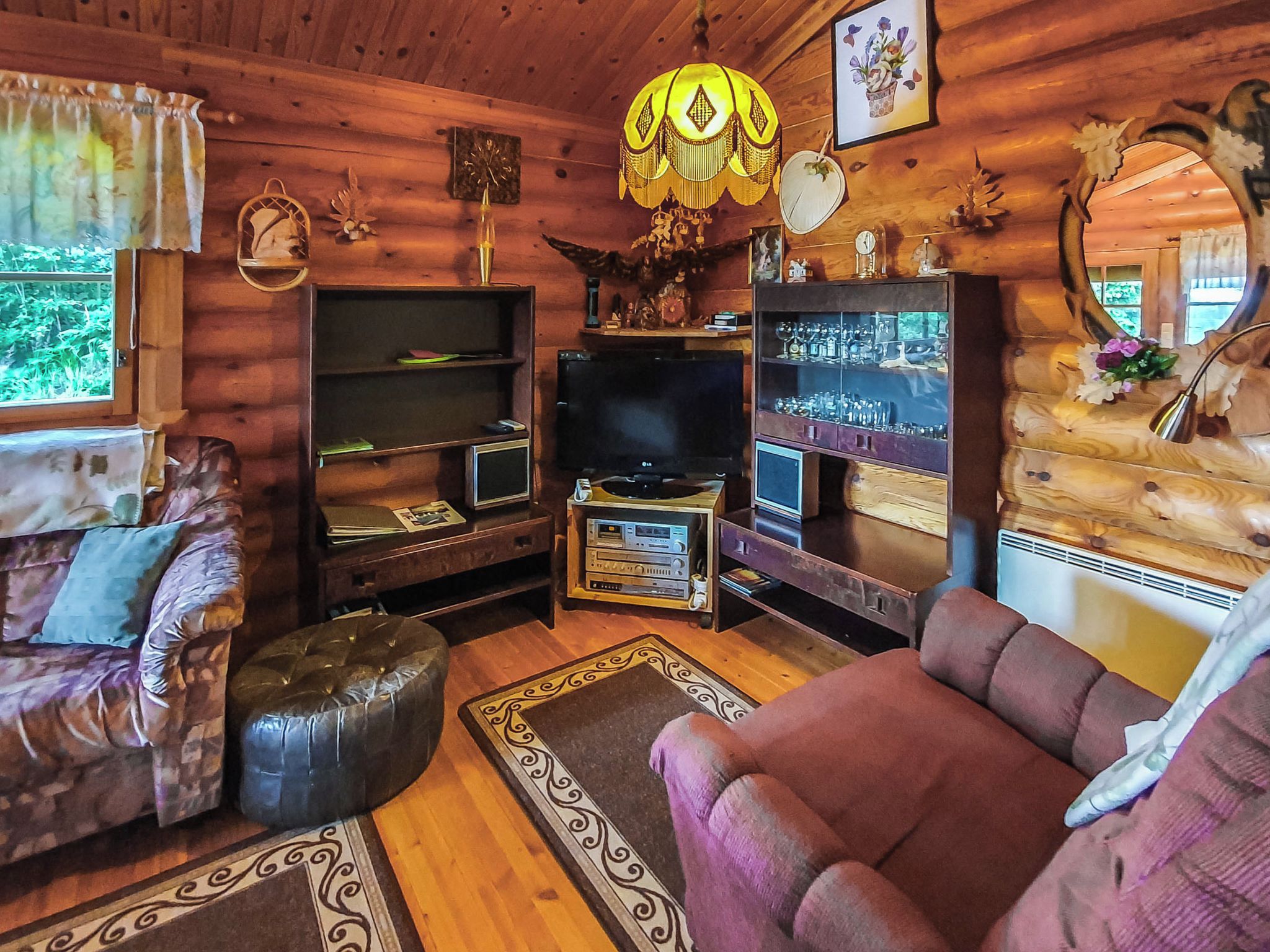 A cozy cabin interior with a wooden interior, a television, a fireplace, and a large window.
