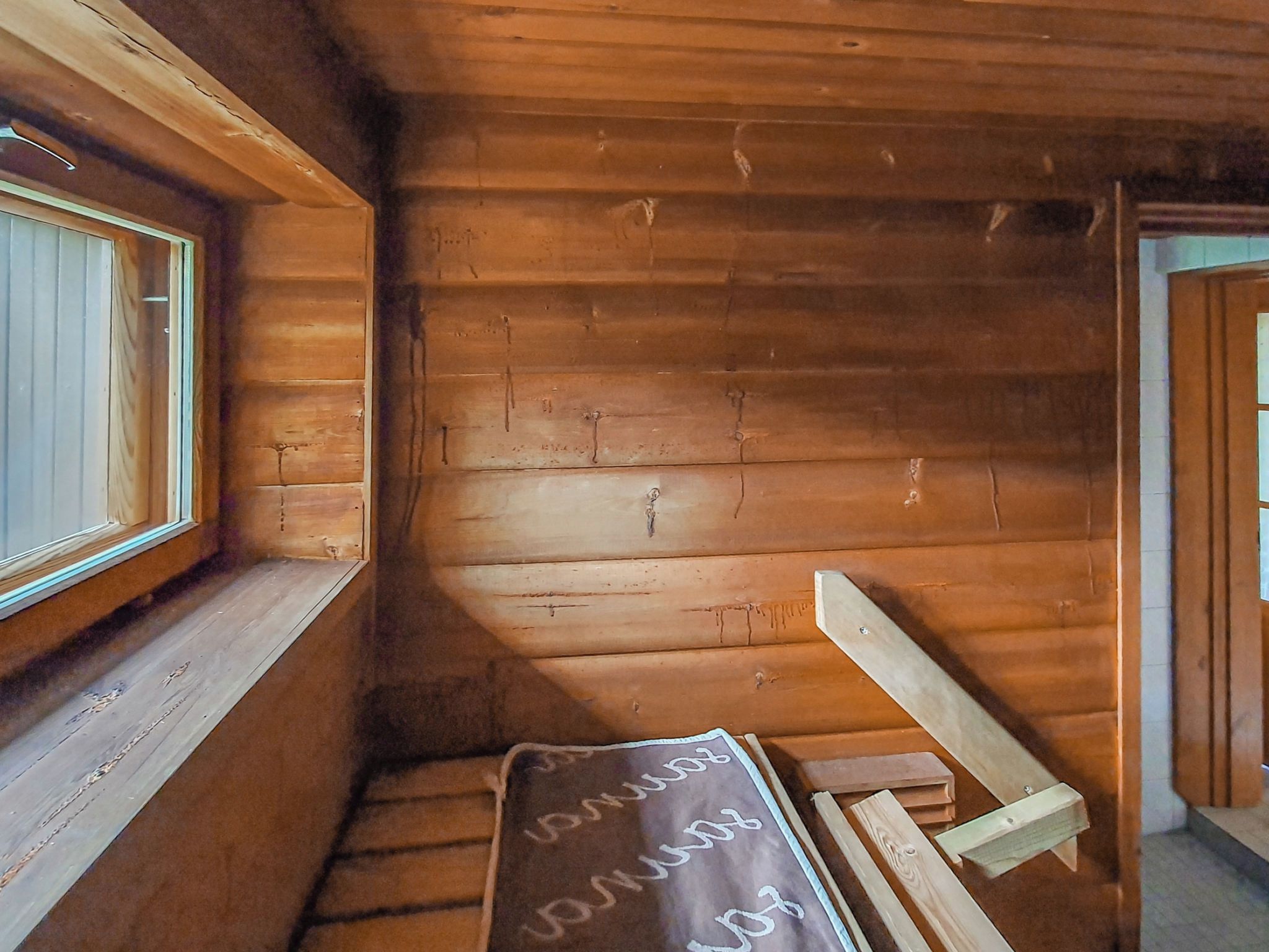 Interno di una baita in legno con una finestra, una panchina e una porta.