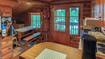 Interno di una baita con tavolo da pranzo in legno, una panca, angolo cottura e finestra con vista sul verde.