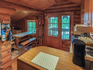 A cabin interior with a wooden dining table, a bench, a kitchen area, and a window with a view of greenery. - Rinne-expertti by Interhome (Ruokolahti)