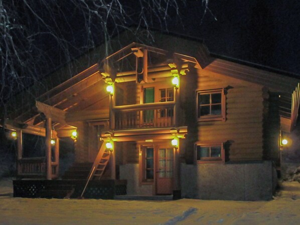 A two-story log cabin with a balcony, a front porch, and a visible staircase leading to the entrance.