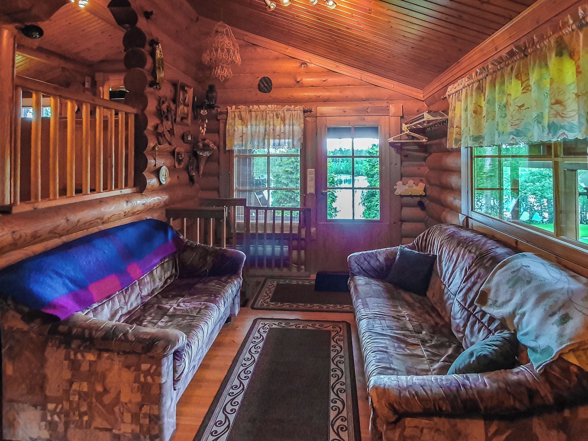 Ein Blockhaushaus-Interieur mit zwei Sofas, einer Holzbalkendecke und Blick auf grüne Vegetation draußen.