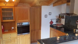 Una cocina con armarios de madera, horno de acero inoxidable, encimera negra y colgador para ollas.