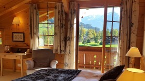 Un dormitorio acogedor con una cama grande, un escritorio y una silla, con vistas panorámicas a la montaña a través de amplias ventanas.